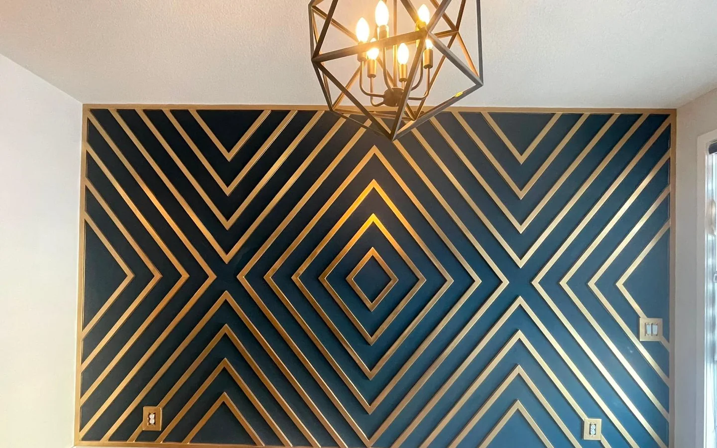 Finished geometric feature wall painted deep teal with gold trim and a matching gold light fixture
