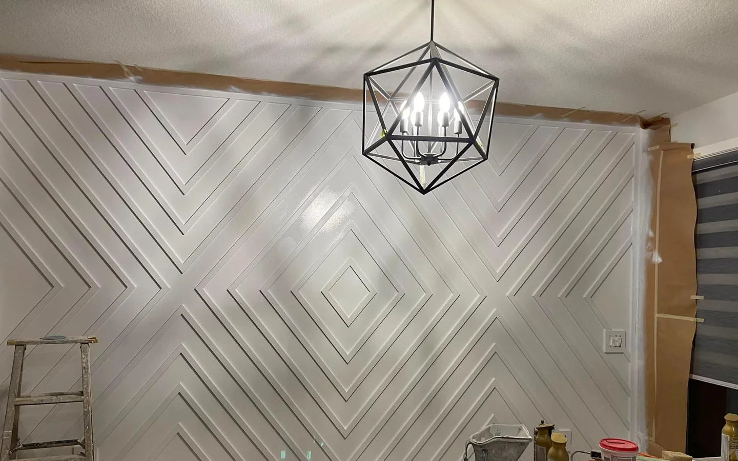 The same feature wall mid-project, primed white with masking paper, drop sheets and a ladder still in place